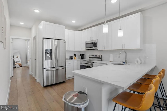 kitchen with sink, kitchen peninsula, decorative light fixtures, stainless steel appliances, and a breakfast bar area