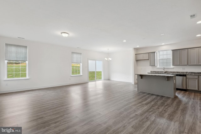 unfurnished living room featuring plenty of natural light, visible vents, dark wood-style flooring, and an inviting chandelier
