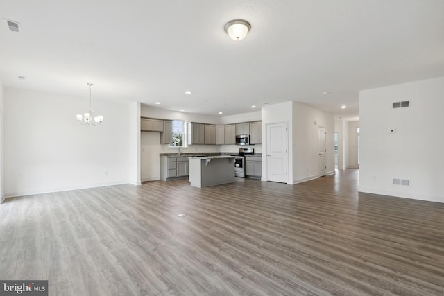 unfurnished living room featuring visible vents, a notable chandelier, and wood finished floors