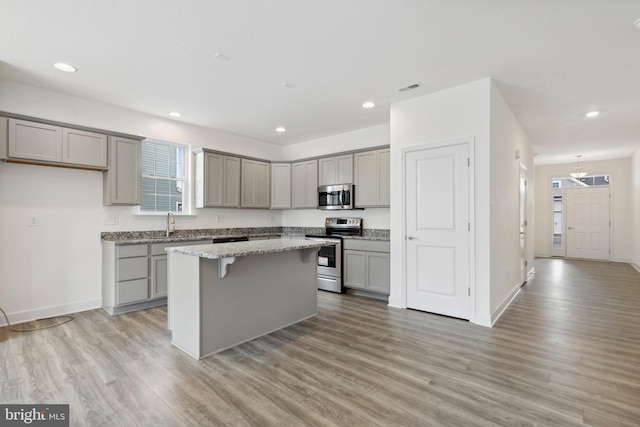 kitchen with light stone counters, appliances with stainless steel finishes, light wood-type flooring, and a kitchen island