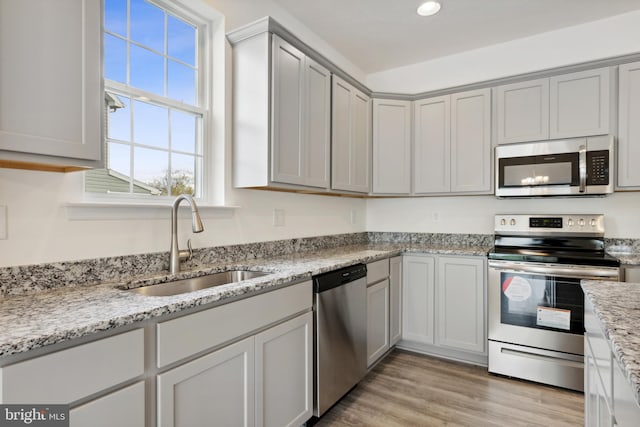 kitchen with appliances with stainless steel finishes, gray cabinetry, light stone countertops, light hardwood / wood-style flooring, and sink