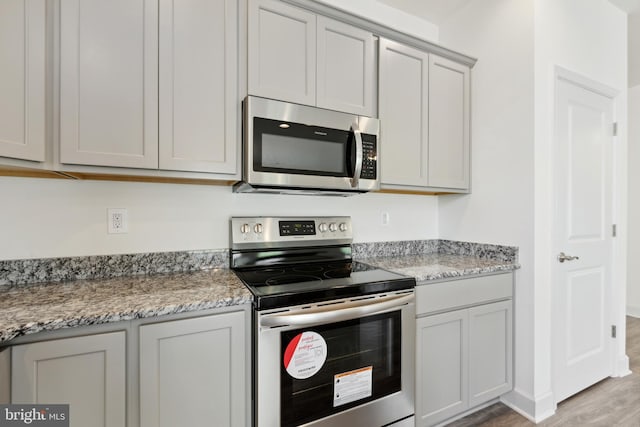 kitchen with gray cabinetry, stainless steel appliances, light wood-style floors, and light stone counters