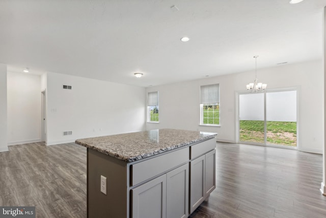 kitchen with light stone counters, hardwood / wood-style flooring, an inviting chandelier, a center island, and decorative light fixtures