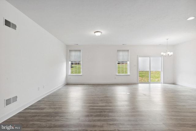 unfurnished room with an inviting chandelier, wood finished floors, and visible vents