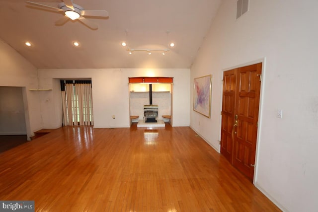 unfurnished living room featuring a wealth of natural light, light hardwood / wood-style floors, a wood stove, high vaulted ceiling, and ceiling fan