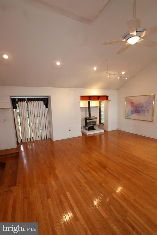 unfurnished living room featuring a wood stove, vaulted ceiling, plenty of natural light, and hardwood / wood-style floors