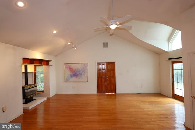 unfurnished living room featuring light hardwood / wood-style floors, a wood stove, and high vaulted ceiling