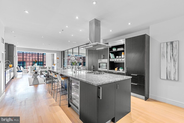 kitchen with a large island, beverage cooler, island range hood, appliances with stainless steel finishes, and light wood-type flooring