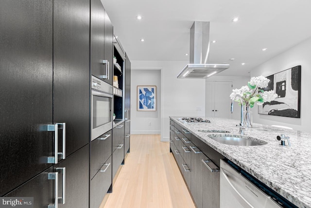 kitchen featuring light stone countertops, sink, stainless steel appliances, light hardwood / wood-style floors, and island range hood