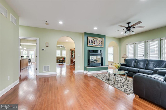 living room featuring wood-type flooring, a multi sided fireplace, and ceiling fan