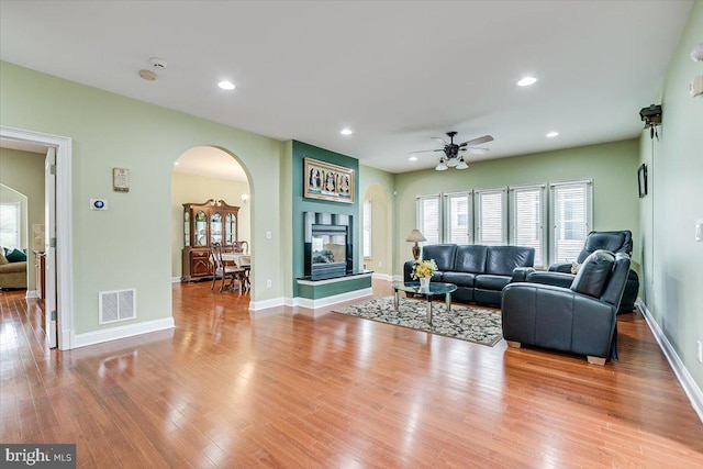 living room featuring ceiling fan, a multi sided fireplace, and light hardwood / wood-style floors