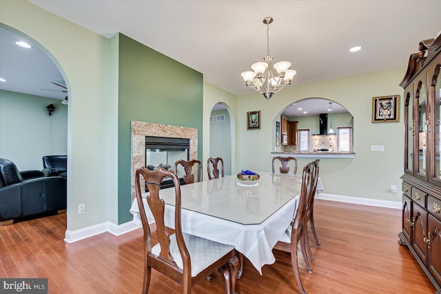 dining area with plenty of natural light, light hardwood / wood-style flooring, a premium fireplace, and a notable chandelier