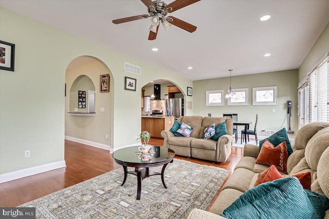 living room featuring ceiling fan with notable chandelier, sink, and wood-type flooring