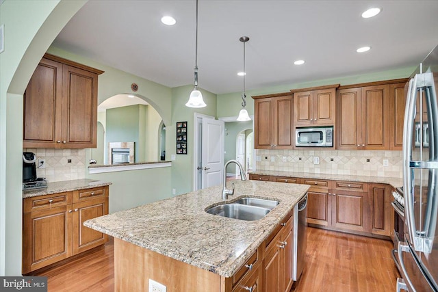 kitchen featuring hanging light fixtures, sink, a kitchen island with sink, light hardwood / wood-style flooring, and appliances with stainless steel finishes