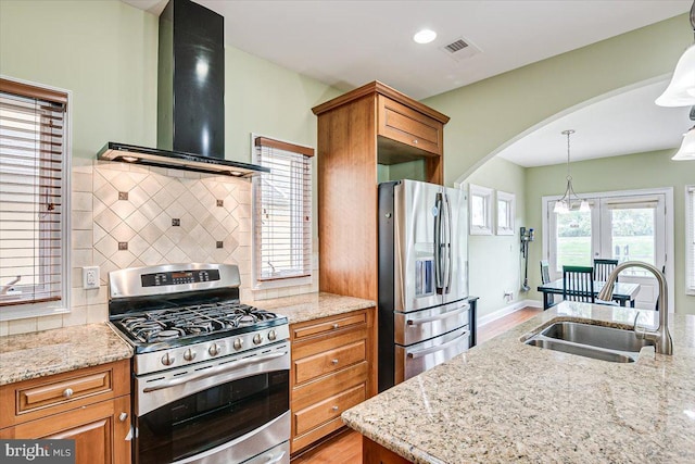 kitchen featuring stainless steel appliances, light stone counters, wall chimney range hood, and sink