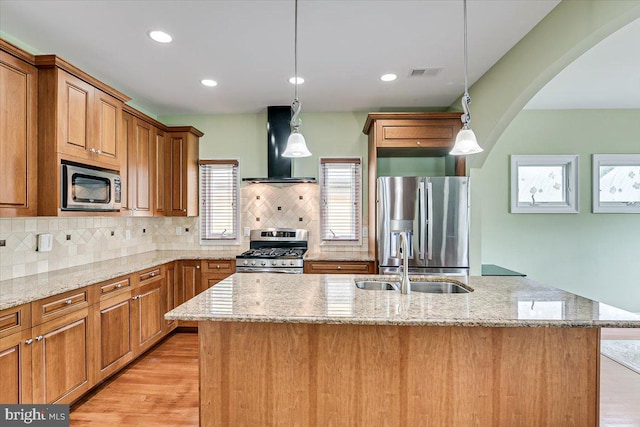 kitchen featuring decorative light fixtures, appliances with stainless steel finishes, sink, and wall chimney range hood