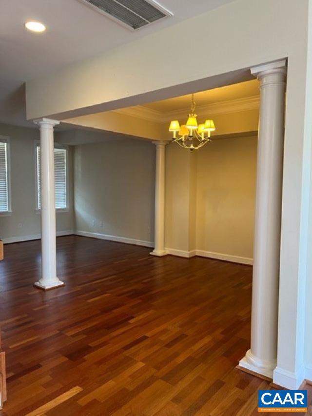 unfurnished dining area featuring ornamental molding, a notable chandelier, dark hardwood / wood-style floors, and ornate columns