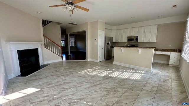 kitchen with appliances with stainless steel finishes, a kitchen island with sink, ceiling fan, and white cabinets