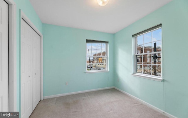 unfurnished bedroom with light carpet, a closet, and multiple windows