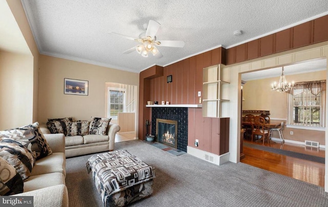 living room featuring ceiling fan with notable chandelier, a tiled fireplace, a textured ceiling, wood-type flooring, and ornamental molding