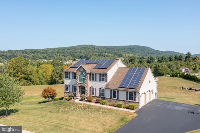 colonial home featuring a front yard, solar panels, and a garage