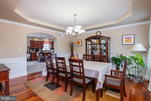 dining space with an inviting chandelier, a raised ceiling, crown molding, and dark hardwood / wood-style flooring