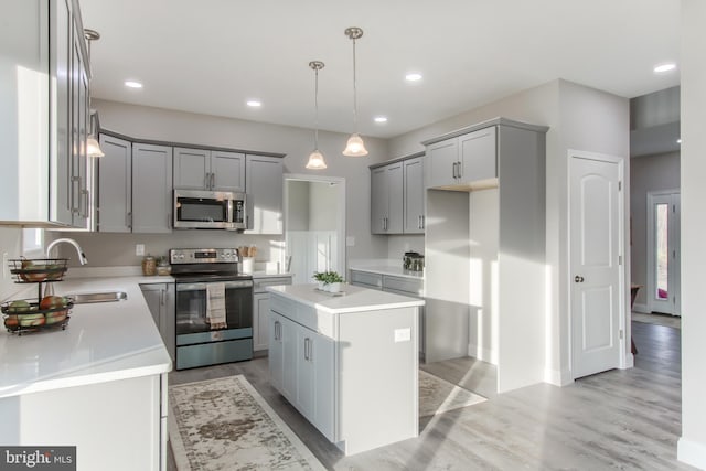 kitchen with gray cabinetry, a kitchen island, pendant lighting, stainless steel appliances, and light hardwood / wood-style flooring