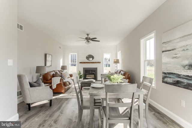 dining space with wood-type flooring, ceiling fan, and a large fireplace