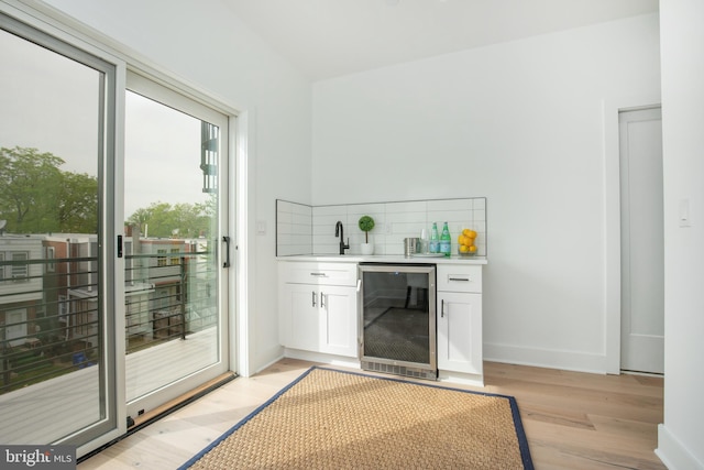 bar featuring decorative backsplash, beverage cooler, white cabinetry, and light hardwood / wood-style floors