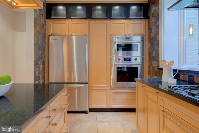 kitchen with appliances with stainless steel finishes, dark stone countertops, light brown cabinets, and tasteful backsplash