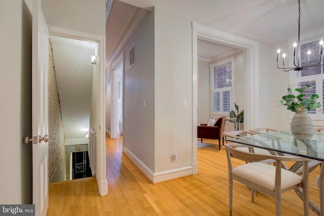 hallway with light wood-type flooring, a chandelier, and crown molding