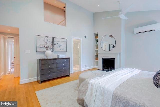 bedroom featuring a wall unit AC, light hardwood / wood-style floors, high vaulted ceiling, ensuite bath, and ceiling fan