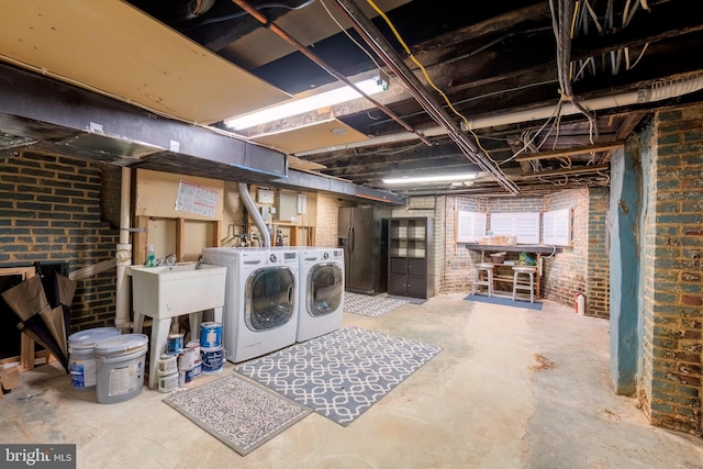 basement featuring brick wall, stainless steel refrigerator with ice dispenser, sink, and washing machine and dryer