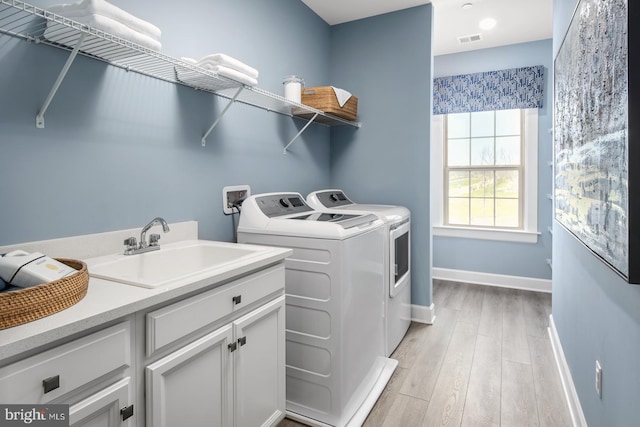 clothes washing area featuring light hardwood / wood-style flooring, washing machine and dryer, cabinets, and sink