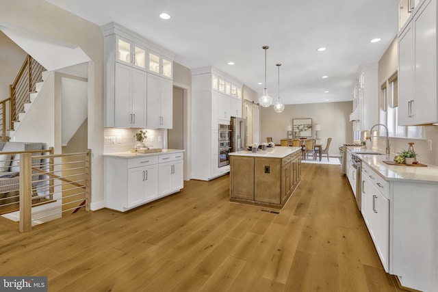 kitchen with decorative light fixtures, light wood-type flooring, a large island, decorative backsplash, and white cabinets