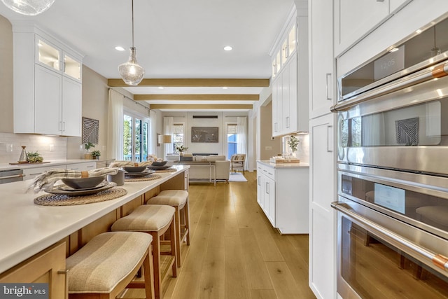 kitchen with pendant lighting, double oven, white cabinets, decorative backsplash, and light hardwood / wood-style floors