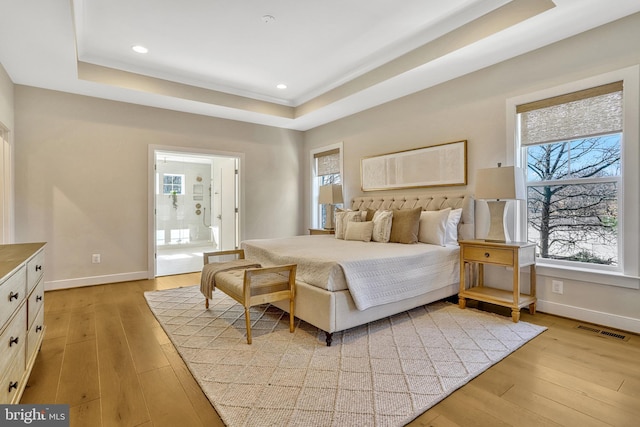 bedroom with ensuite bath, a raised ceiling, and light hardwood / wood-style flooring