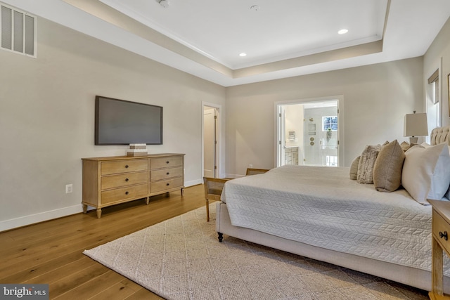 bedroom with wood-type flooring, ensuite bath, and a tray ceiling