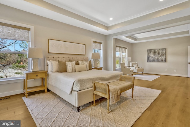 bedroom with crown molding, a tray ceiling, and light hardwood / wood-style floors