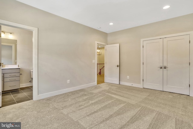 unfurnished bedroom featuring ensuite bath, a closet, and dark colored carpet