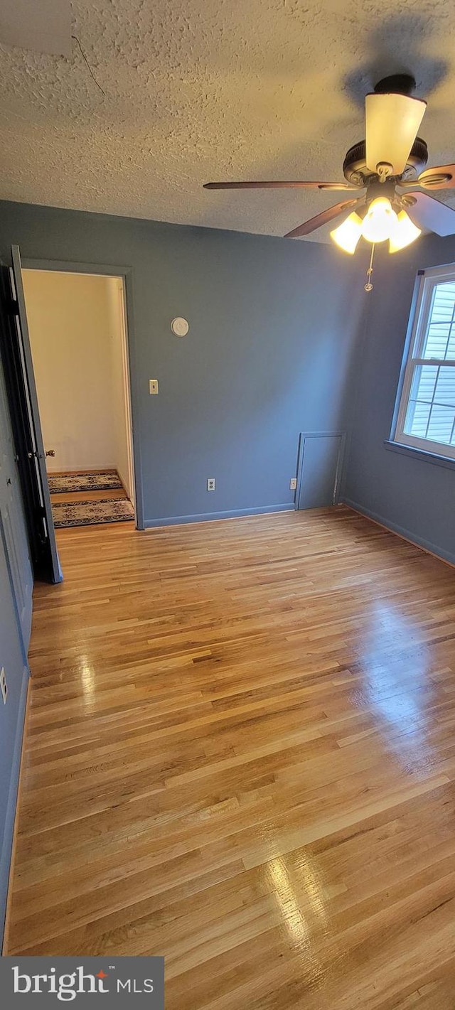 empty room featuring light wood-type flooring, a textured ceiling, and ceiling fan