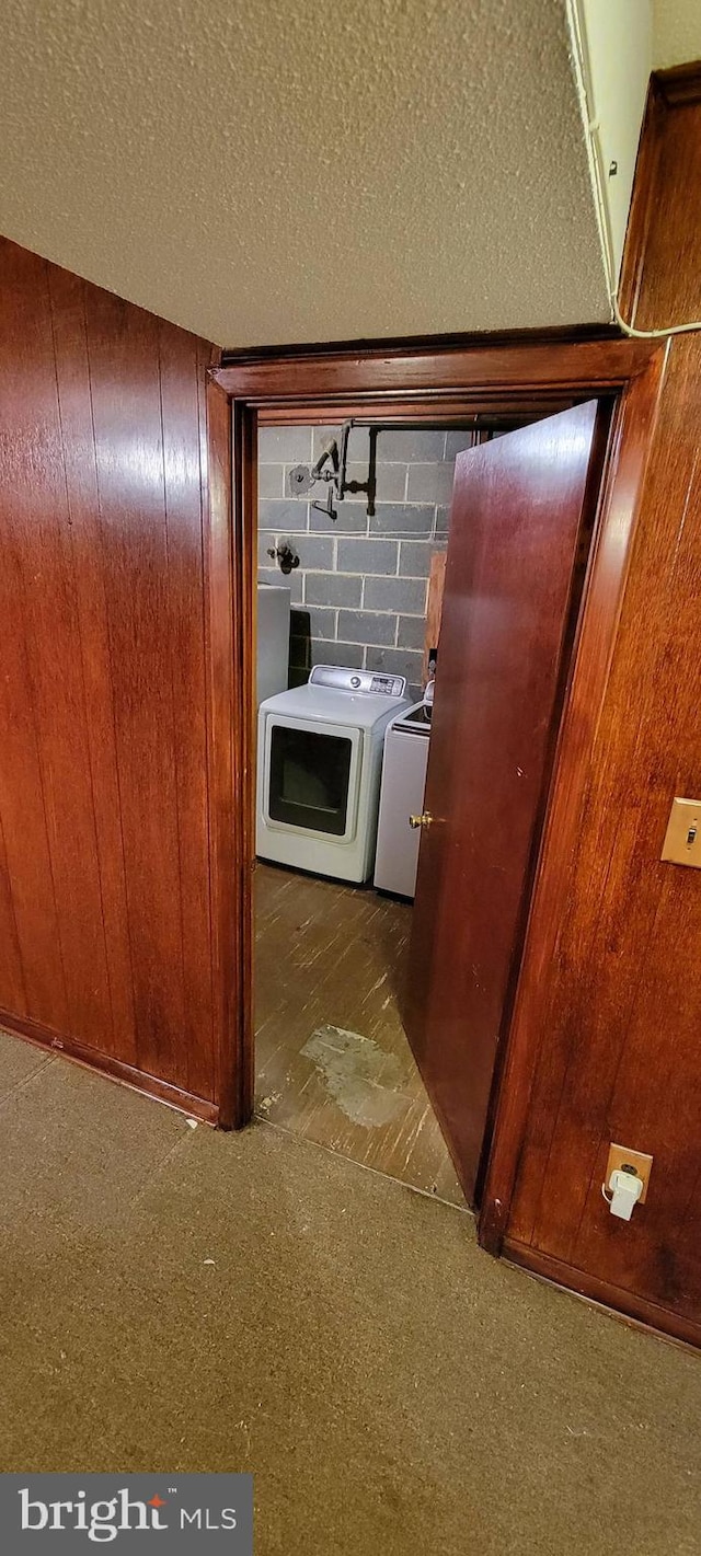 hallway with dark carpet, a textured ceiling, wood walls, and independent washer and dryer