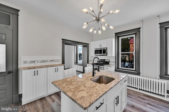 kitchen featuring appliances with stainless steel finishes, white cabinetry, radiator, a kitchen island with sink, and sink