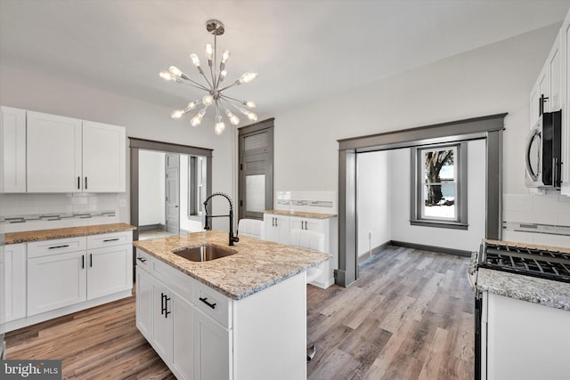 kitchen featuring white cabinetry, tasteful backsplash, white range with gas cooktop, a kitchen island with sink, and sink