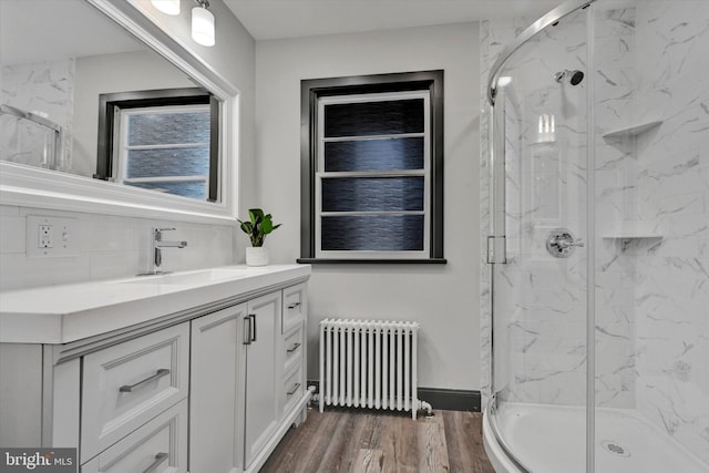 bathroom with wood-type flooring, radiator, backsplash, walk in shower, and vanity