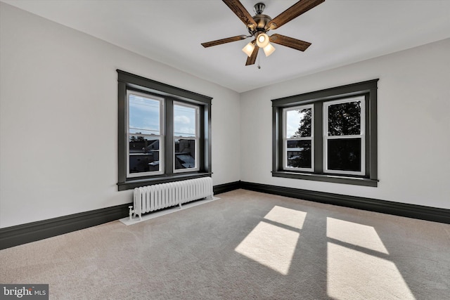 unfurnished room featuring carpet floors, radiator, ceiling fan, and plenty of natural light