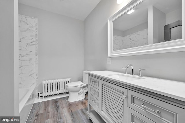 full bathroom with hardwood / wood-style floors, radiator heating unit, vanity, tiled shower / bath, and toilet