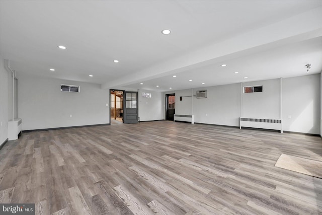 unfurnished living room featuring light wood-type flooring, an AC wall unit, and radiator heating unit