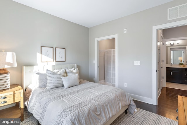 bedroom with a spacious closet, ensuite bath, a closet, and dark hardwood / wood-style floors