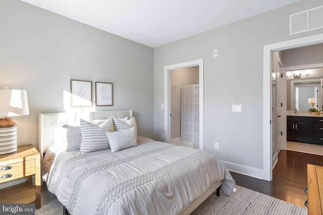 bedroom featuring wood finished floors, ensuite bathroom, a walk in closet, baseboards, and visible vents
